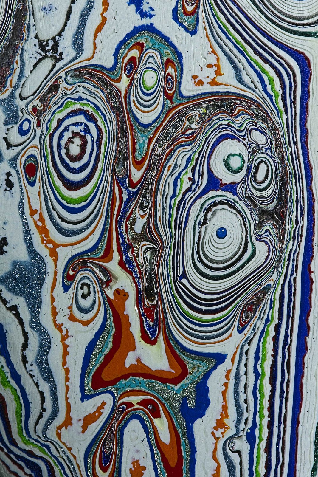 Fordite, also known as Motor Agate, is a unique automotive enamel material with an interesting history. The original layered automotive paint slag “rough” was made incidentally, years ago, by the now extinct practice of hand spray-painting multiples of production cars in big automotive factories. 
The oversprayed paint in the painting bays gradually built up on the tracks and skids that the car frames were painted on. Over time, many colorful layers built up there. These layers were hardened repeatedly in the ovens that the car bodies went into to cure the paint. Some of these deeper layers were even baked 100 times. 
Eventually, the paint build-up would become obstructing, or too thick and heavy, and had to be removed. As the story goes, some crafty workers with an eye for beauty realized that this unique byproduct was worth salvaging. It was super-cured, patterned like psychedelic agate, and could be cut and polished with relative ease! 