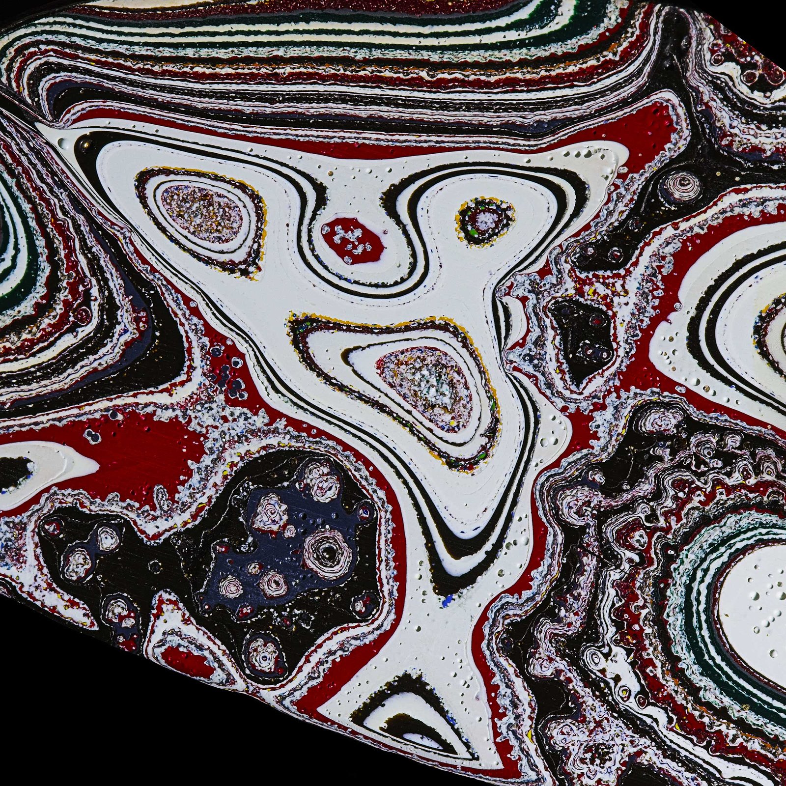 Fordite, also known as Motor Agate, is a unique automotive enamel material with an interesting history. The original layered automotive paint slag “rough” was made incidentally, years ago, by the now extinct practice of hand spray-painting multiples of production cars in big automotive factories. 
The oversprayed paint in the painting bays gradually built up on the tracks and skids that the car frames were painted on. Over time, many colorful layers built up there. These layers were hardened repeatedly in the ovens that the car bodies went into to cure the paint. Some of these deeper layers were even baked 100 times. 
Eventually, the paint build-up would become obstructing, or too thick and heavy, and had to be removed. As the story goes, some crafty workers with an eye for beauty realized that this unique byproduct was worth salvaging. It was super-cured, patterned like psychedelic agate, and could be cut and polished with relative ease! 